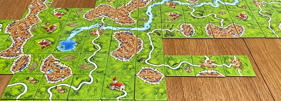 Płytki do gry planszowej Carcassonne przedstawiające średniowieczne miasta, drogi, pola i klasztory ułożone na stole podczas rozgrywki.